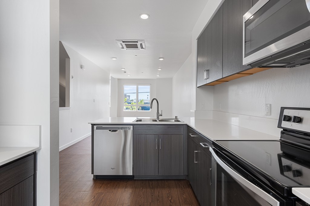 A modern kitchen with dark wood floors and stainless steel appliances.